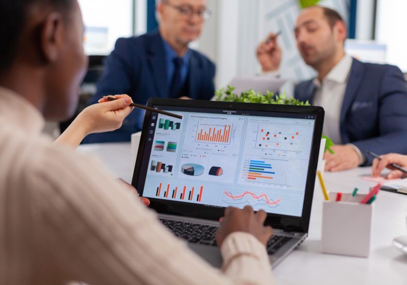Equipa multidisciplinar numa reunião de trabalho sobre energias limpas, com maquetes de turbinas eólicas, painel solar fotovoltaico e análise de mapas topográficos.