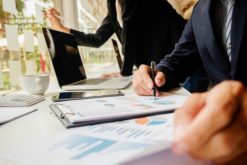 Consultores a analisar gráficos financeiros e relatórios de desempenho num escritório com computadores portáteis.